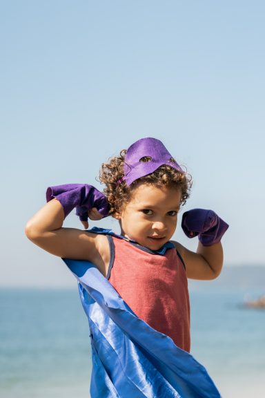 Estime de soi Estime de soi : enfant déguisé en super-héros avec une cape, montrant ses muscles au bord de la mer